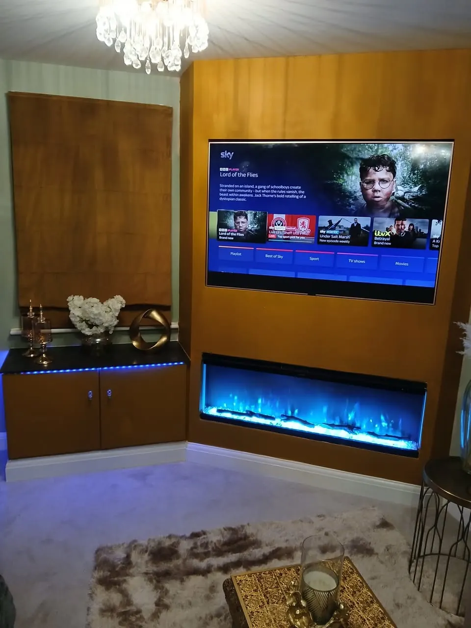 Finished media wall with inset electric fire and chandelier-lit living room