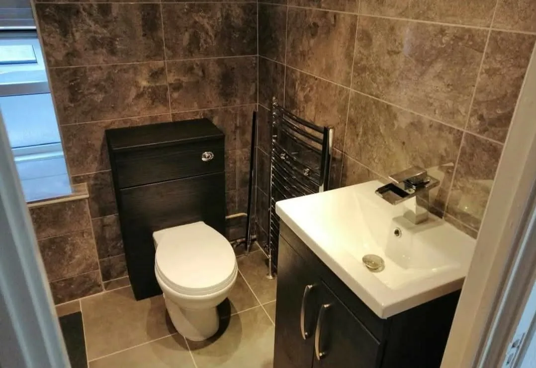 Fully tiled cloakroom with vanity unit, basin and heated towel rail